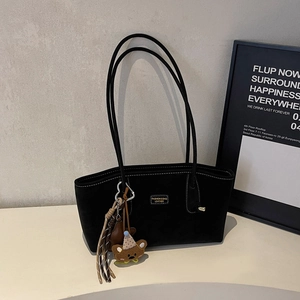 Close-up of black suede tote bag with contrast stitching and teddy bear keychain
