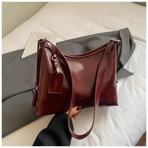 Detail shot of a burgundy oil-wax leather tote bag with stylish brand tag and buckle
