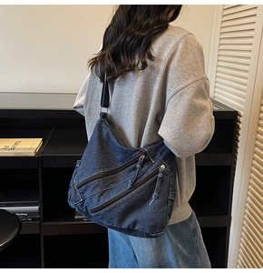 Detail of blue denim hobo bag featuring triple diagonal zipper pockets and washed texture