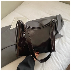 Detail of a dark brown glossy tote bag with metal buckle and shoulder strap