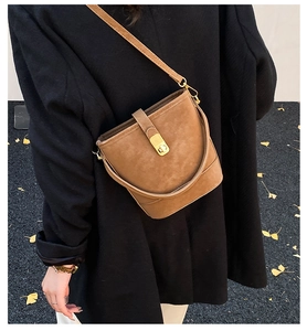 Braune Wildleder-Eimertasche mit Goldschloss vor schwarzem Blazer und Herbstblättern