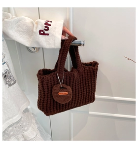 Detail of dark brown waffle knit tote bag featuring a handmade charm with orange leather tag