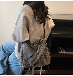 Détail du sac hobo en denim délavé avec plusieurs fermetures éclair et une large bandoulière
