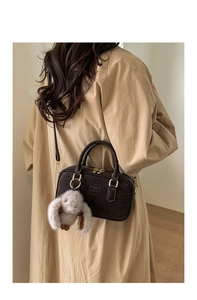 Detail of dark coffee matte pillow bag with long-ear rabbit plush charm on a khaki coat