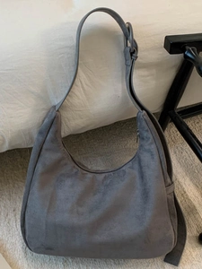 Sac hobo minimaliste en daim gris avec bandoulière réglable dans un décor de chambre