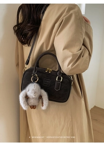 Detail of retro mini Boston bag in coffee suede with plush rabbit charm on beige trench coat