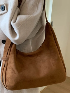Sac hobo en daim marron avec large bandoulière porté avec un manteau beige élégant