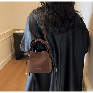 Close-up of brown textured bucket bag with woven handle and gold metal details