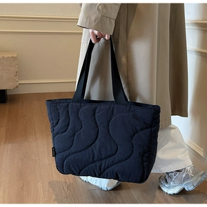 Detail of black quilted tote bag with wave stitching held by a model in casual outfit