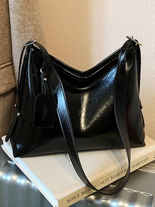 Minimalist black glossy tote bag with adjustable strap on a textured book surface