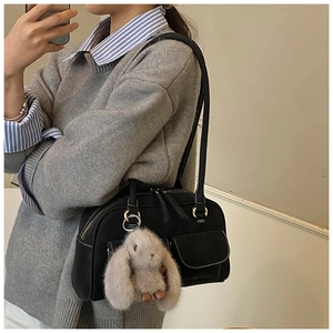 Detail of black retro shoulder bag with white contrast stitching and plush bunny pendant