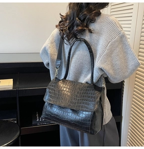 Detail of black crocodile texture tote bag with wide strap worn by a model
