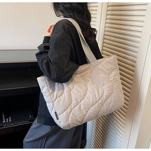 Woman carrying large light gray quilted puffer tote bag with stylish wave pattern detail