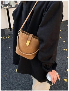 Detailansicht einer braunen Bucket-Bag mit goldenem Drehverschluss vor Straßenhintergrund