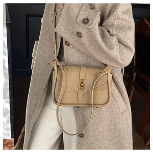 Dettaglio della borsa a tracolla in pelle color crema con fibbia dorata su cappotto