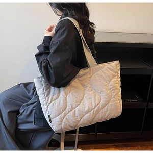 Side view of a light grey quilted tote bag with wave stitching and a woven brand tag