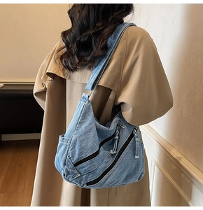 Detail view of denim tote bag with diagonal zippers and side pockets on khaki trench coat