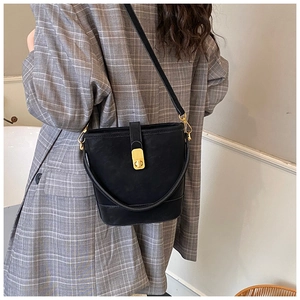 Detail einer schwarzen Eimer-Tasche aus Leder mit Goldverschluss auf grauem Blazer