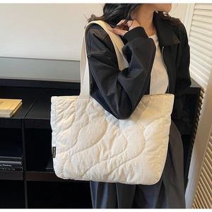 Close-up of the large quilted pattern and brand tag on a cream-white tote bag
