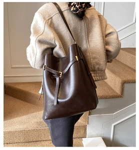 Detail of dark brown oil wax leather bucket bag with slim strap and gold buckle