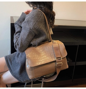 Detail of dark brown crocodile embossed shoulder bag with chic wide textile strap and gold hardware