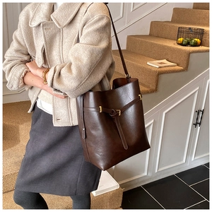 Detail of dark brown leather tote bag with gold buckle in a stylish indoor setting