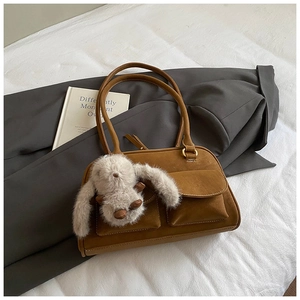 Detail of a brown suede underarm bag with square pockets and a plush bunny charm