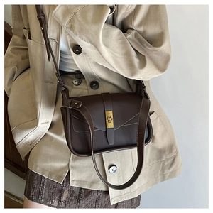 Dettaglio di una borsa a tracolla marrone scuro con chiusura a scatto dorata su una modella