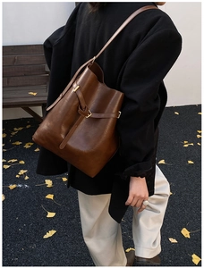 Lifestyle shot of a brown vintage leather bucket bag styled with a chic black coat