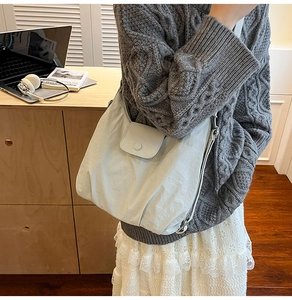 Detail of greyish-white pleated nylon tote bag with snap button and textured fabric surface