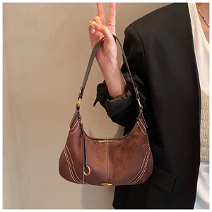 Macro shot of dark brown suede half-moon bag with contrast stitching and gold metal buckle