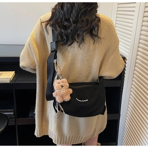 Detail of black suede tote bag with white branding text and a brown plush bear charm