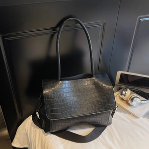 Detail shot of black crocodile pattern leather tote bag with wide strap and laptop
