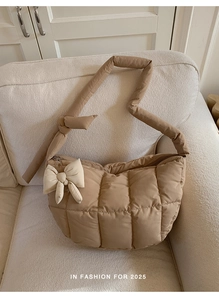 Détail du sac fourre-tout matelassé kaki avec un pendentif nœud crème sur un canapé