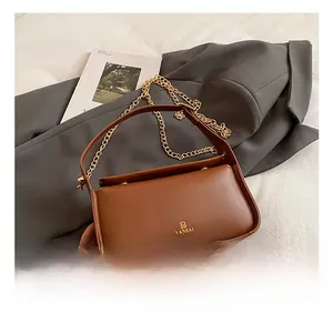 Détail du sac bandoulière en cuir marron avec chaîne dorée et logo métallique élégant