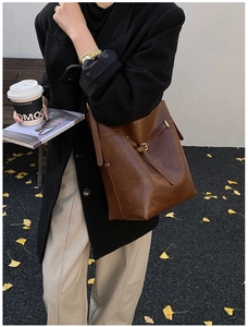Detail view of brown leather bucket bag side featuring adjustable strap and metal buckle