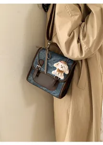 Close-up of vintage denim and leather messenger bag featuring a cute plush dog pendant