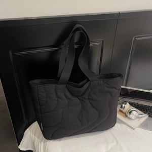 Detail shot of black quilted nylon tote bag featuring wavy stitching and brand side label