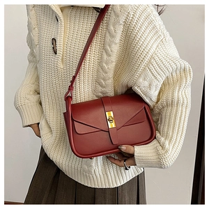 Dettaglio borsa a tracolla bordeaux con chiusura girevole dorata su maglione bianco