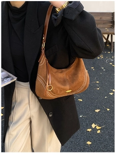 Close-up of brown suede underarm bag with white contrast stitching and metal hardware details