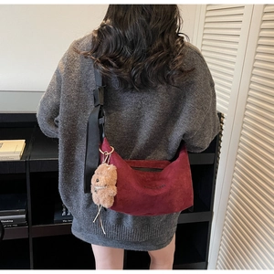Detail of burgundy suede tote bag with wide shoulder strap and plush bear charm