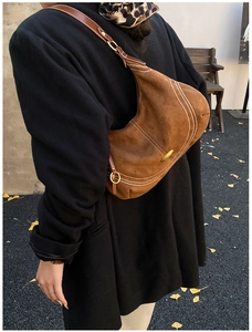 Brown suede hobo bag with white stitching and gold hardware shown on a model