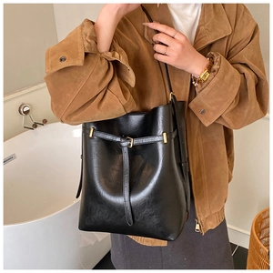 Detail of glossy black leather bucket bag with strap buckle shown on model in modern setting