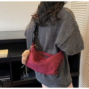 Detail of burgundy suede tote bag with black strap and plush bear charm on model