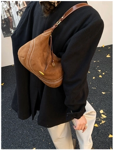 Close-up of brown suede hobo bag featuring white wavy stitching and slim leather strap