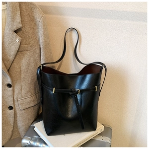 Detail view of black leather bucket bag featuring a gold buckle belt and soft grain texture