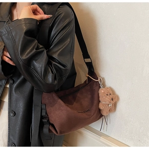 Close-up of deep brown suede tote bag with embroidered logo and plush bear charm