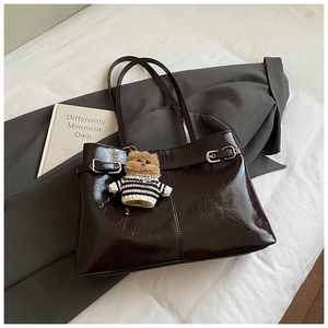 Détail du cabas en cuir brillant marron foncé avec boucle argentée et charm ours en peluche