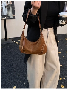 Detail of dark brown suede crescent bag with white contrast stitching and gold buckle