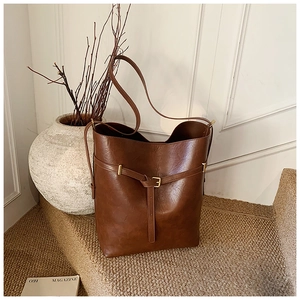 Close-up of a vintage brown leather bucket bag with metal buckle on a beige carpet